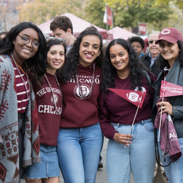 A group of five female students dressed in UChicago and maroon clothing pose together at a Homecoming block party.