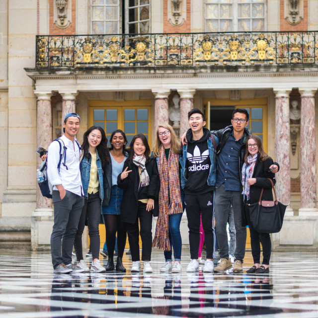 Students stand in front of a classical style building with balconies.