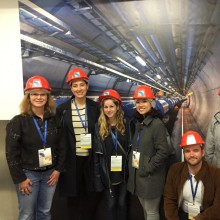 A group of students in hard hats stand in front of a post at the European Center for Nuclear Research in Switzerland.