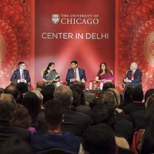 A group of speakers participate in a panel onstage behind a decorative backdrop.
