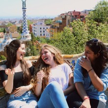 Three students laugh together on a bench in Parque Guell in Barcelona.