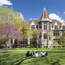 A group of students sit in a circle outside in front of a gothic-style building.
