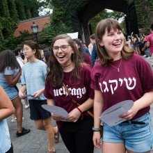 Two smiling female students walk amongst a group of students wearing maroon UChicago shirts in English and Hebrew.