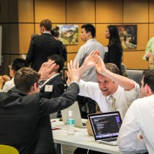 A group of three male students around a table high five.