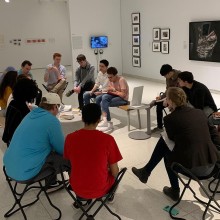 A class meets in a gallery in the smart museum, with pictures and other exhibits nearby.