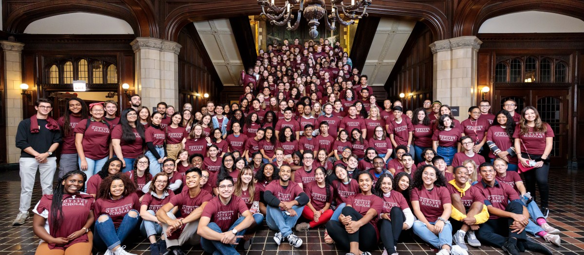 A large group of students are pictured on a wooden staircase wearing shirts that say "University of Chicago Odyssey Scholar"