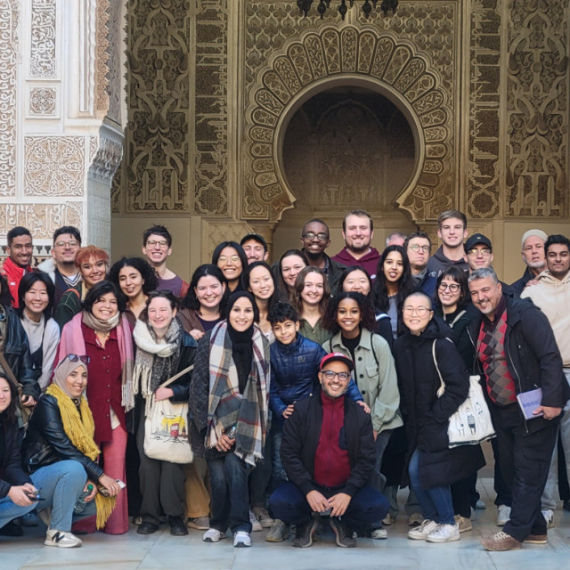 A large group of students stands in front of a Middle-Eastern looking building.