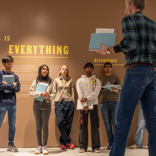 A professor stands in front of a group of students at a Smart Museum exhibit titled "Poetry is Everything."