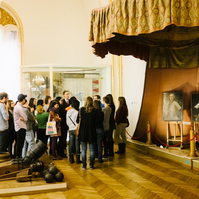 A group of students stand around a professor as he discusses an exhibit in a museum in Vienna.