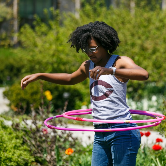 A female student hula hoops amongst flowers on a sunny day.