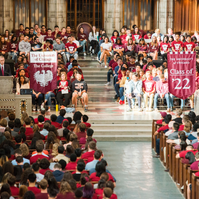 A large group of students sit in the pews of a chapel listening to a speaker. Flags for The College and the Class of '22 are displayed.