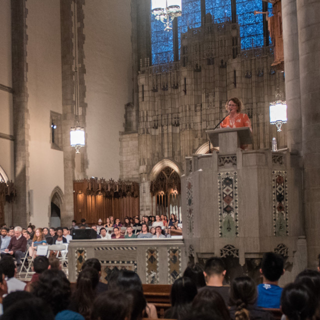 A speaker stands at the pulpit of Rockefeller chapel with a full audience.