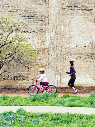 Sabina Shaikh runs behind her daughter as she rides a bikes near a large stone wall.