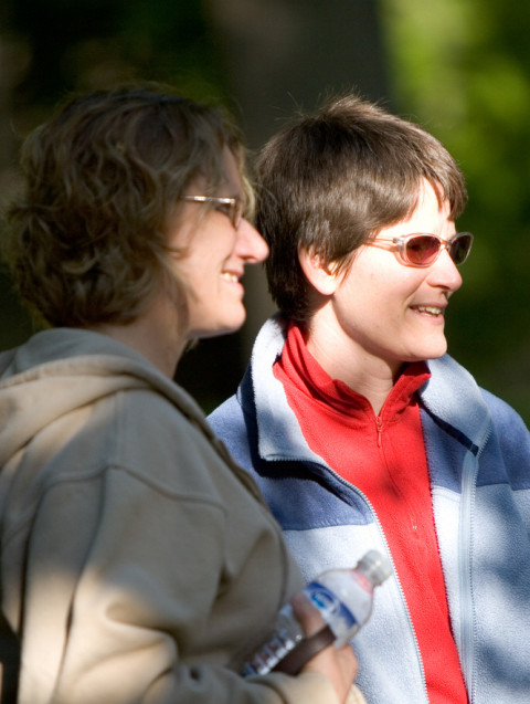 Two people are shown outside on a sunny day. The person on the right (Kathy Forde) is wearing red-tinted sunglasses.