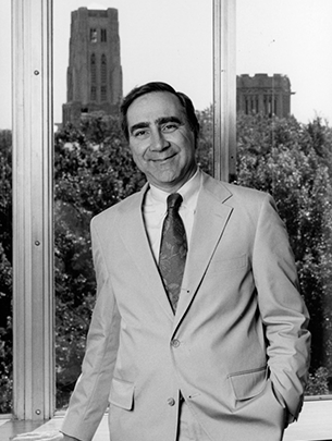 A black and white portrait of Hugo Sonnenschein in his office with gothic buildings shown through the window behind him.