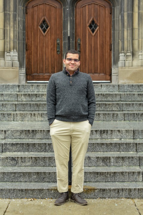 Boone Ayala stands outdoors in front of steps and doors.