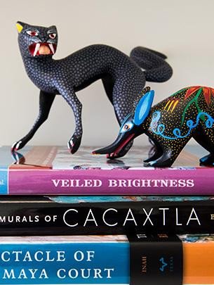 Two brightly colored figurines of fantastical animals are shown atop a stack of books.