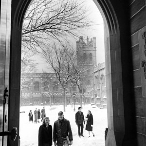 Black and white photo of students walking through snow covered quad surrounded by gothic buildings.