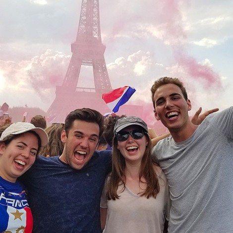 Four smiling people in front a cloud of pink dust and the silhouette of the Eiffel tower.
