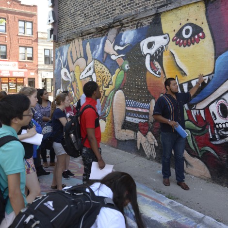 A group of students stand in front of a mural on a wall in a neighborhood in Chicago.