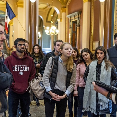 A group of students stands listening to a tour guide in an elaborate state capitol building.