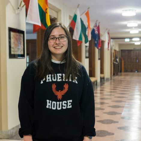 Lungstrom stands smiling proudly in a Phoenix House sweatshirt in the bright hallway of International House.