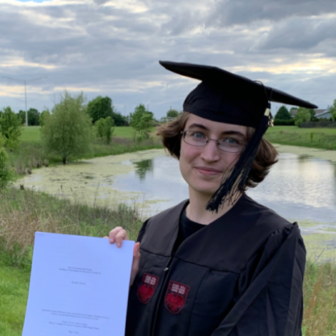 A portrait of Emily Stevens holding a paper copy of their BA thesis